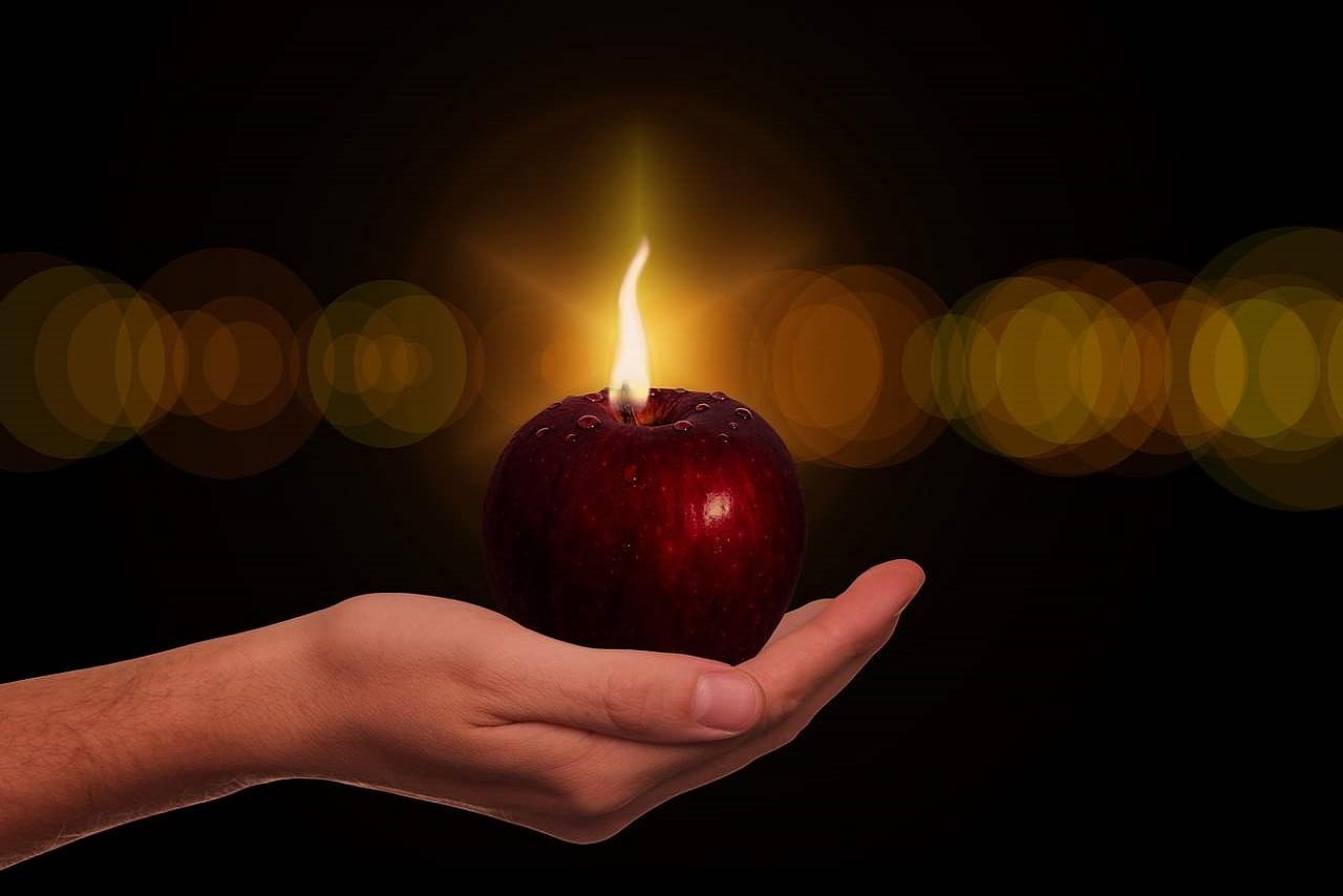 une pomme rouge dont le pédoncule est en feu est posée dans la paume d'une main