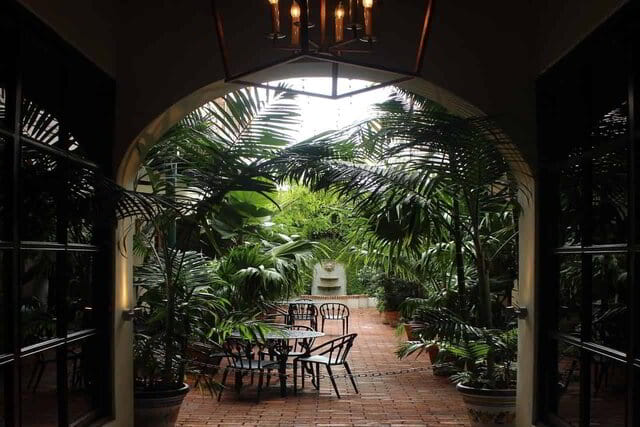 sous un porche on voit un luxuriant jardin avec des tables