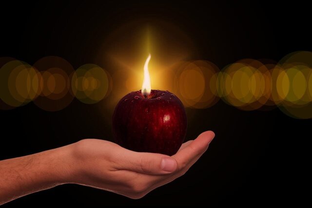 une pomme rouge dans la paumme de la main son pedoncule est une flamme